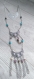 Un sautoir avec des pendentifs styles égyptien et un autre pendentif vers le haut en métal argenté qui fait croire à un deuxième collier le tout avec des perles pour toute la beauté 