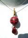Pendentif constitué d'une perle ronde en pâte fimo, à motif rose rouge et noire sur fond rouge suspendue par un fermoir et avec une goutte en verre rouge.