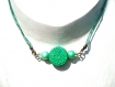 Pendentif constitué d'une perle ronde plate en pâte polymère, à motif vert foncé, vert anis et bleu ciel entourée de perles en bois vert clair nacré